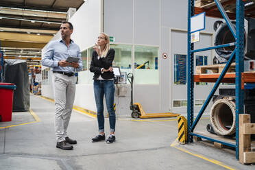Ein Geschäftsmann hält ein digitales Tablet, während eine Unternehmerin in einer Fabrik daneben steht - DIGF13371