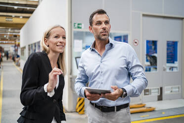 Smiling female entrepreneur and businessman looking away while holding digital tablet standing at industry - DIGF13373