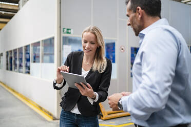 Eine Kollegin benutzt ein digitales Tablet, während ein Geschäftsmann in einer Fabrik neben ihr steht - DIGF13377