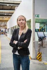 Confident blond female entrepreneur with arms crossed standing in industry - DIGF13378