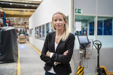 Smiling blond businesswoman with arms crossed standing in industry - DIGF13379