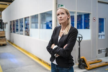 Thoughtful businesswoman with arms crossed standing in factory - DIGF13380