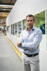 Male entrepreneur with arms crossed standing in factory - DIGF13382