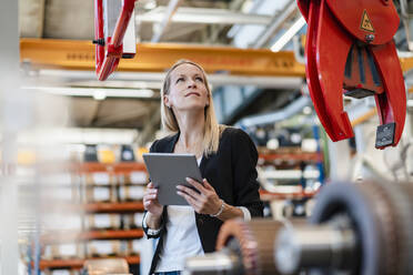 Geschäftsfrau prüft Klaue, während sie ein digitales Tablet in einer Fabrik hält - DIGF13402