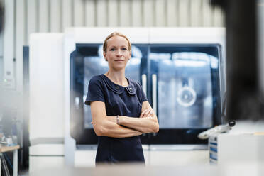 Smiling female businesswoman with arms crossed standing against door in industry - DIGF13412