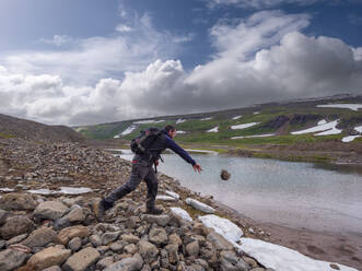 Männlicher Wanderer wirft einen Stein in den Fluss - LAF02561