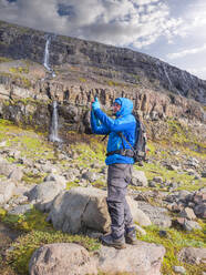 Männlicher Wanderer macht Smartphone-Fotos vor einem abgelegenen Wasserfall - LAF02563