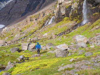 Male hiker walking between boulders along Icelandic valley - LAF02564