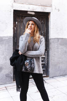 Thoughtful stylish woman with hat looking away while standing on street - JMPF00642