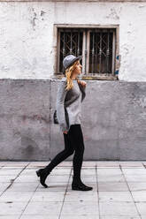 Junge Frau mit Hut geht an einem Gebäude vorbei auf die Straße - JMPF00643