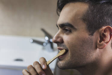 Young man brushing teeth with bamboo toothbrush - MGRF00059