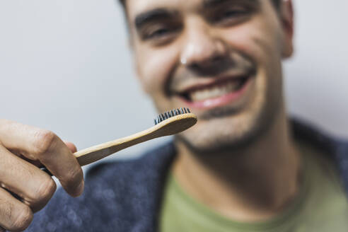 Lächelnder Mann beim Zähneputzen mit Bambuszahnbürste - MGRF00064