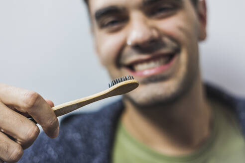 Smiling man brushing teeth with bamboo toothbrush - MGRF00064