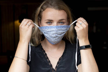 Porträt einer jungen blonden Frau, die eine blaue Gesichtsmaske aufsetzt. - MINF15250