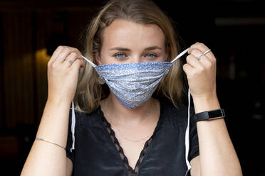 Portrait of young blond woman putting on blue face mask. - MINF15250