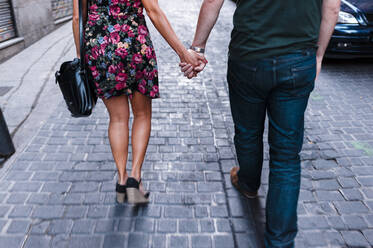 Girlfriend and boyfriend holding hands walking on street in city - JMPF00658