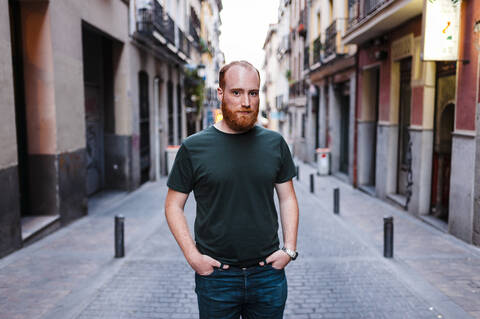 Bearded man with hands in pockets standing on street in city stock photo
