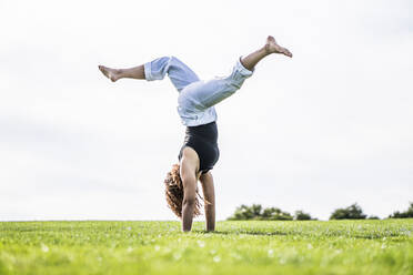 Weibliche Athletin übt Rad auf Gras im Park gegen den klaren Himmel - ABAYF00024