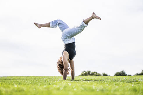 Weibliche Athletin übt Rad auf Gras im Park gegen den klaren Himmel - ABAYF00024