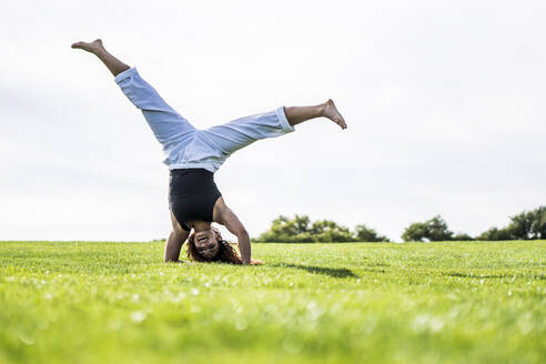 Sportlerin macht Handstand auf Gras im Park gegen klaren Himmel - ABAYF00025