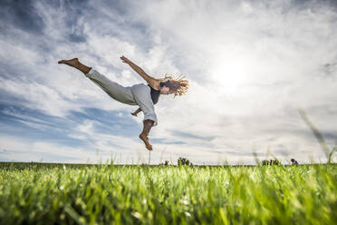 Weibliche Athletin springt in der Luft über Gras im Park gegen bewölkten Himmel - ABAYF00026