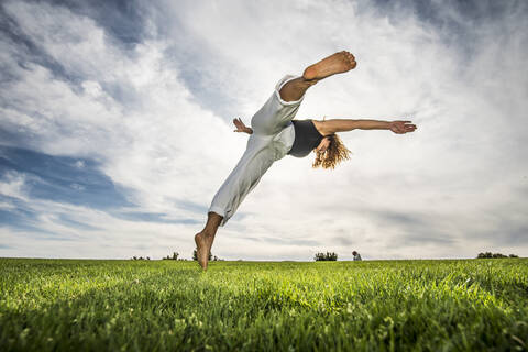 Female acrobat doing movement in park against cloudy sky stock photo