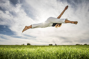 Sportlerin macht akrobatische Aktivität im Park gegen bewölkten Himmel - ABAYF00028