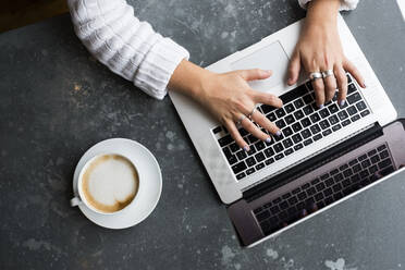 High angle view of woman sitting alone at a cafe table with a laptop computer, working remotely. - MINF15305