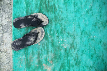 Nahaufnahme von sandfarbenen schwarzen Flip Flops auf türkisfarbener Bodenmatte. - MINF15309