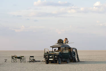 Ein Mann steht auf einem Geländewagen, der auf den Makadikadi-Salzpfannen in Botswana geparkt ist. - MINF15321