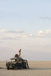 Ein Mann steht auf einem Geländewagen, der auf den Makadikadi-Salzpfannen in Botswana geparkt ist. - MINF15322