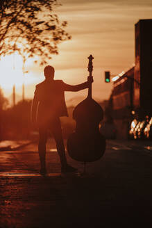 Männlicher Musiker, der einen Kontrabass hält und an der Straße steht - GMLF00846