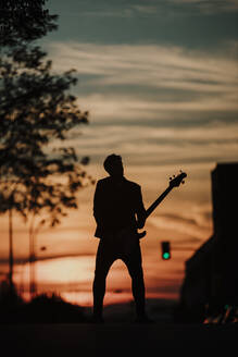 Silhouette eines Musikers, der Bassgitarre spielt und auf der Straße steht - GMLF00848