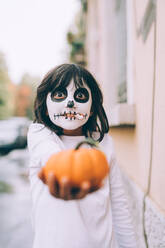 Girl at Halloween with face paint, holding out pumpkin - CUF56569