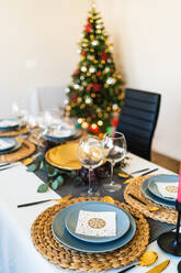Festlich gedeckter Tisch neben geschmücktem Weihnachtsbaum mit leuchtenden Girlanden vor der Weihnachtsfeier - ADSF17638