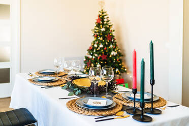 Festlich gedeckter Tisch neben geschmücktem Weihnachtsbaum mit leuchtenden Girlanden vor der Weihnachtsfeier - ADSF17640