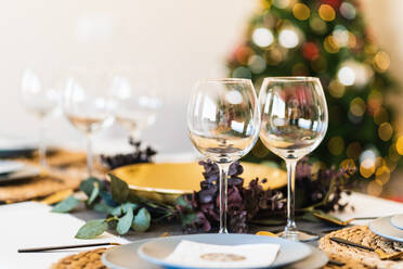 Esstisch mit Gläsern und Tellern vor einem verschwommenen leuchtenden Weihnachtsbaum am Weihnachtsabend zu Hause - ADSF17641