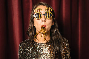 Content female wearing black glamour dress and fancy sunglasses having fun at party while standing on golden background - ADSF17676