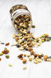 Jar of raisins, peanuts, cashew nuts, almonds, soybeans, sunflower seeds and pumpkin seeds spilled on wooden background - LVF09071