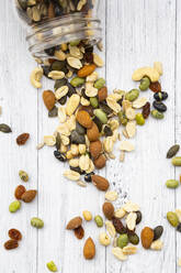 Glas Rosinen, Erdnüsse, Cashewnüsse, Mandeln, Sojabohnen, Sonnenblumenkerne und Kürbiskerne verschüttet auf hölzernen Hintergrund - LVF09072