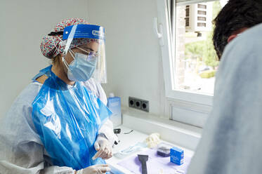 Zahnmedizinische Fachkräfte mit Schutzmaske und Gesichtsschild bei der Arbeit im Stehen in der Klinik während Covid-19 - JCMF01641