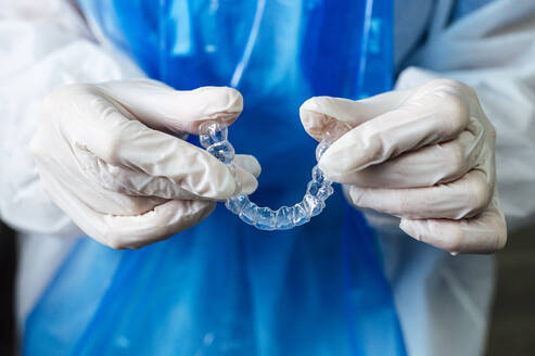 Doctor holding transparent dental aligner while standing at clinic - JCMF01649