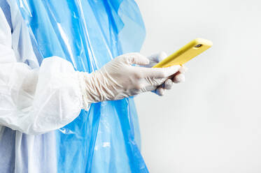 Orthodontist wearing protective workwear using mobile phone while standing in clinic - JCMF01655