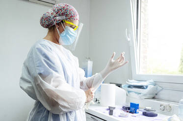 Arzt in Arbeitsschutzkleidung mit Handschuh in der Klinik während Covid-19 - JCMF01669