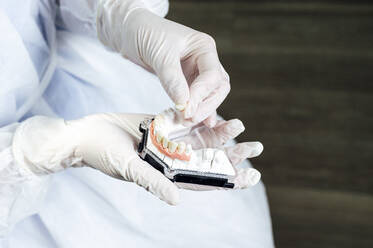 Dentist wearing protective workwear making dentures while standing in clinic - JCMF01670