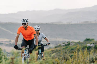 Seriöse Profi-Radfahrer mit Helm und Sonnenbrille fahren im Sommer beim Training im Hochland bergauf - ADSF17700