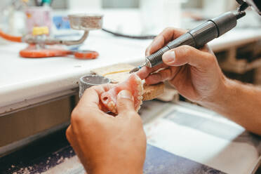 Unrecognizable male technician working in lab and using polishing machine for producing denture - ADSF17730