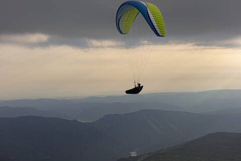 Aerial view of male paraglider soaring above mountains at dusk stock photo