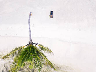 Malediven, Kaafu Atoll, Luftaufnahme eines Mannes, der sich im Liegestuhl am Sandstrand der Insel Huraa entspannt - KNTF05914