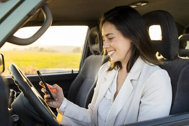Glückliche junge Frau, die während einer Autoreise ihr Smartphone im Auto benutzt - AFVF07578